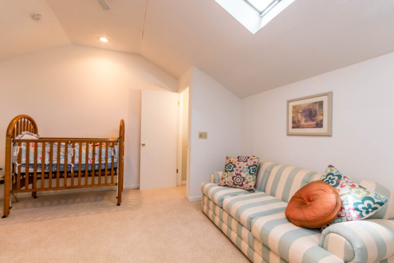 a cozy room with a crib, a striped couch, and bookshelf