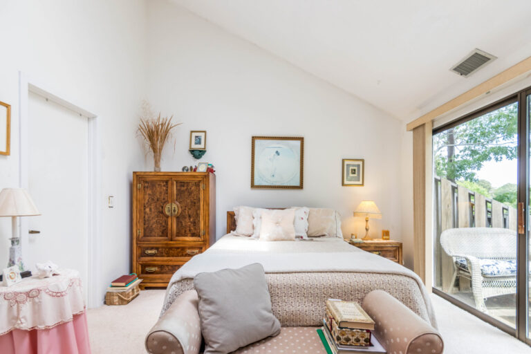 Cozy bedroom with a bed, vintage armoire, and a view of trees through large windows.