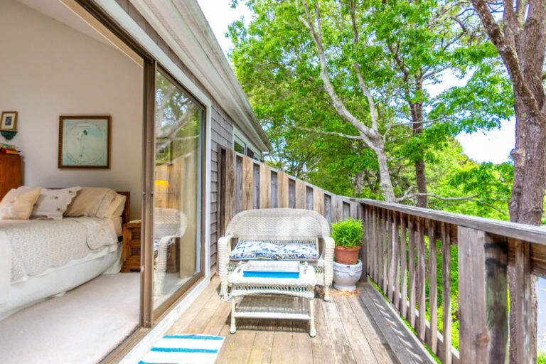 Cozy bedroom with a bed, vintage armoire, and a view of trees through large windows.