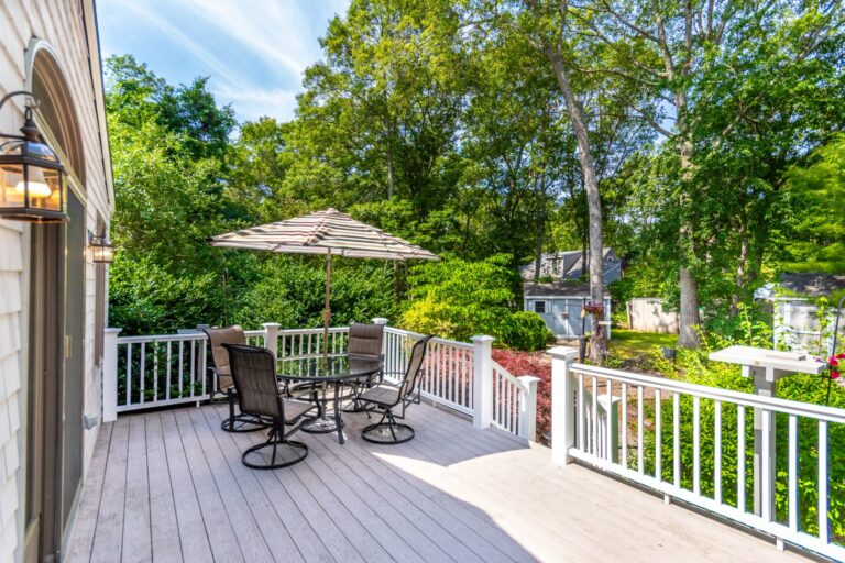 a view of a deck with chairs and table surrounded by trees and plants