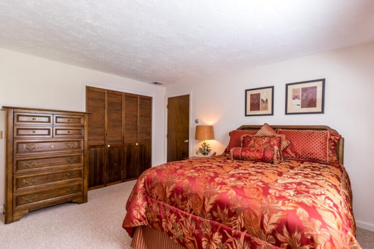primary bedroom with a bed with red sheet and wooden furnitures