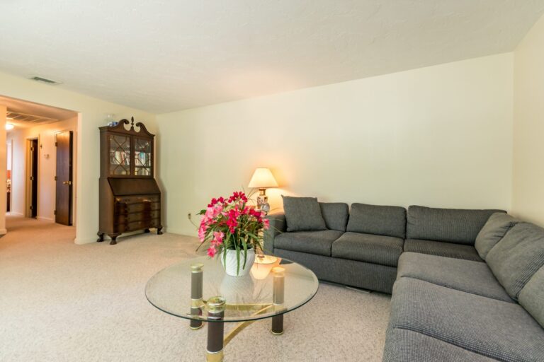 a spacious living room with an L shape couch, tables and plants