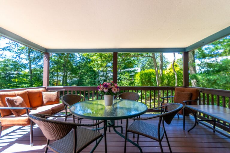 a covered deck with metal furnitures and views of the foliage