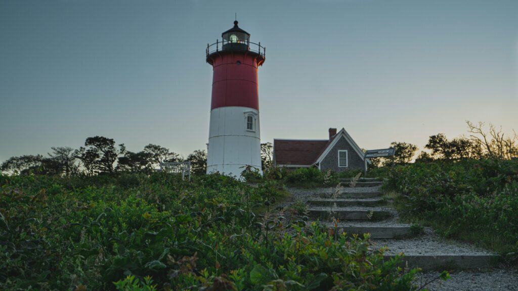 red and white lighthouse near a white house under a blue sky