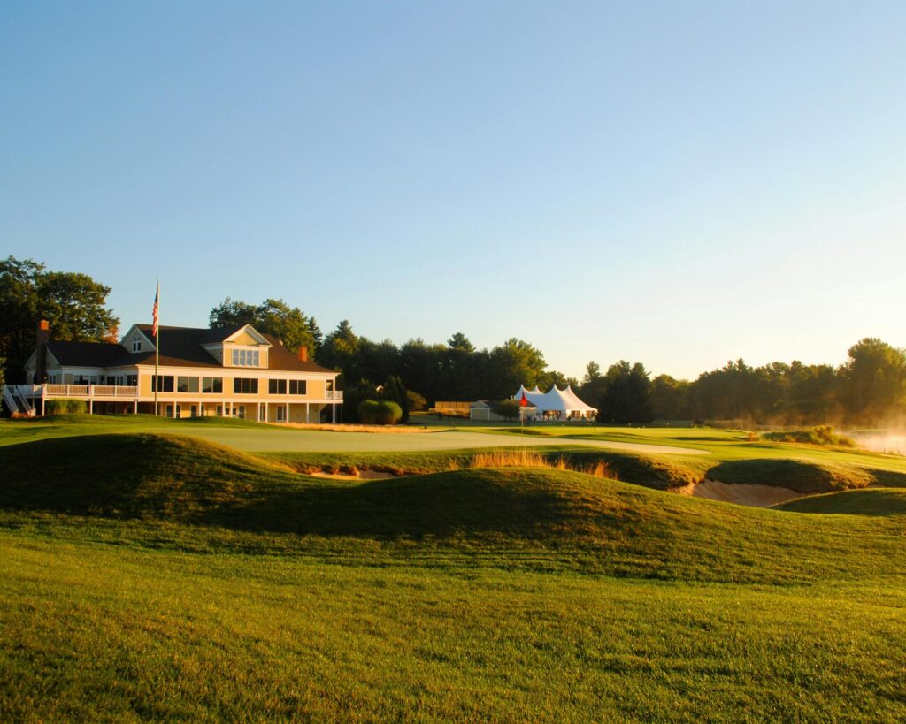 Cottage on grassy hill near golf course under cloudless blue sky.