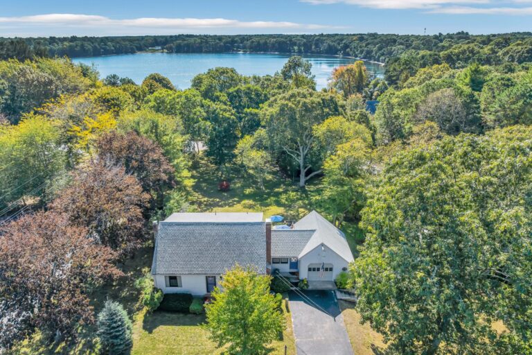 a waterfront Cape Cod home featuring a detached garage and a scenic pond