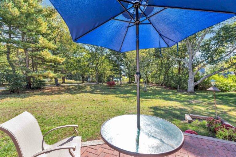 a chair and a round tempered glass top patio table wwith a blue market umbrella
