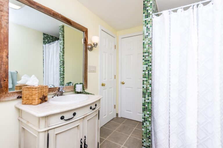 A bright bathroom with a white sink, large mirror reflecting a window, and grey towels hanging on the wall
