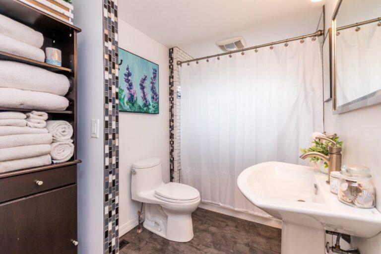 A small bathroom featuring a white pedestal sink and toilet, and decorative mosaic tile accents