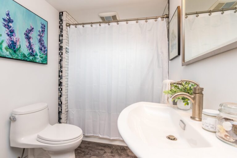A small bathroom featuring a white pedestal sink and toilet, and decorative mosaic tile accents