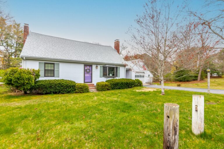 Cape Cod-style house with light-colored siding and a detached garage